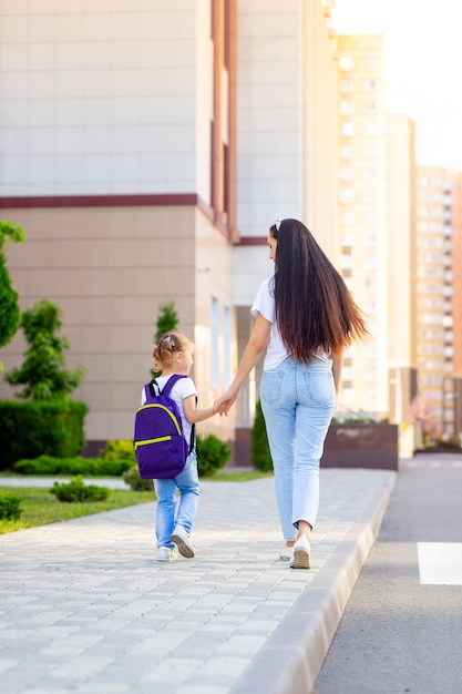 El primer día de clases, un padre lleva a una niña a una colegiala con una mochila de la mano a la primera clase y de regreso a la escuela.