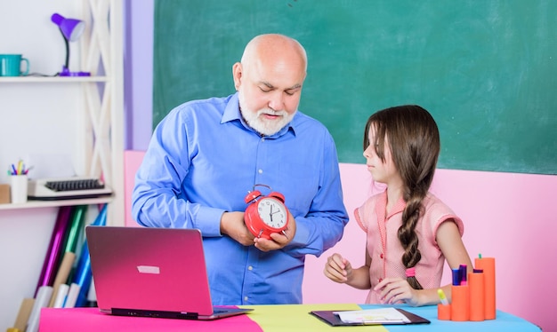 Primer día de otoño. Tiempo de estudiar. lección escolar en línea. blogs de educación. De vuelta a la escuela. pequeña niña con estudio de tutor de hombre en la computadora. profesor maduro ayuda al alumno con el reloj. romper la alarma. Mañana.