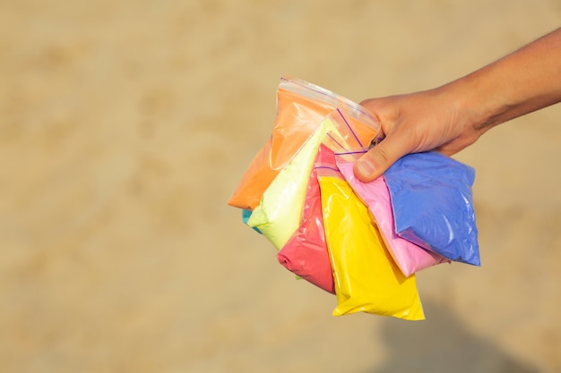 Primer disparo de mano femenina sosteniendo bolsas de pintura colorida seca Holi sobre fondo de arena. Espacio para texto