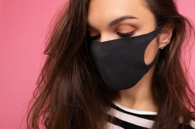 Primer disparo de una mujer hermosa joven en una máscara protectora de virus reutilizable en la cara contra el coronavirus aislado en la pared de fondo rosa
