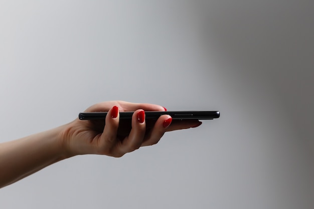 Primer disparo de una mujer que muestra el teléfono móvil aislado sobre fondo blanco. Mano femenina sosteniendo un teléfono inteligente moderno. Mano que muestra la pantalla de un teléfono blanco.