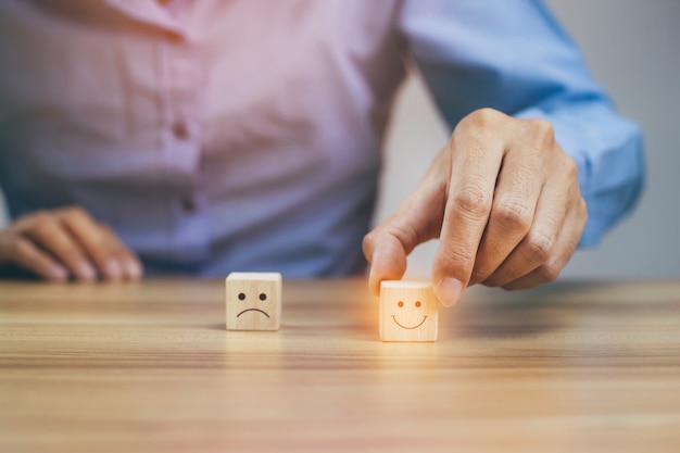 Primer empresario elegir cara sonriente e icono de cara triste borrosa en cubo de madera