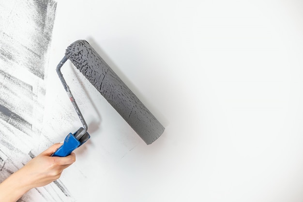 El primer femenino de la mano pinta una pared en gris. El concepto de reparación, cambio, diseño.