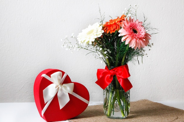 Primer de flores coloridas en el tarro en la servilleta rústica y una caja en forma de corazón con el fondo blanco. Concepto de san valentín