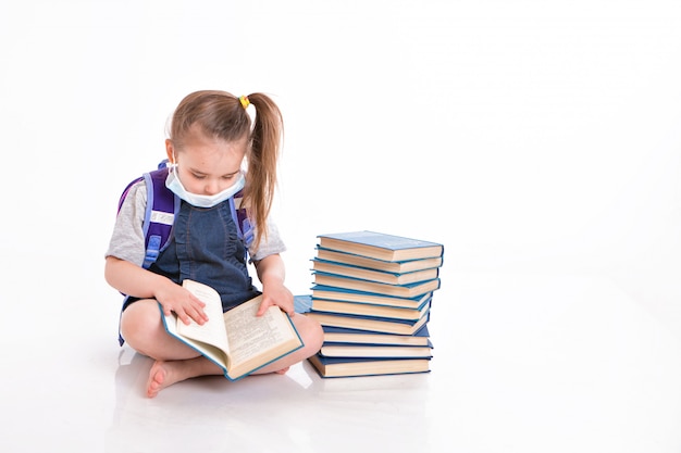 Foto primer grado aprende a leer. una niña en el hogar a distancia. niño con una máscara médica lee un libro. el estudiante está haciendo la tarea.