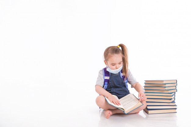 primer grado aprende a leer. una niña en el hogar a distancia. Niño con una máscara médica lee un libro.