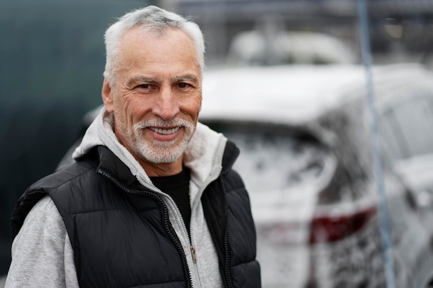 Primer hombre canoso senior sonriendo mirando a la cámara en la estación de lavado de autos de autoservicio