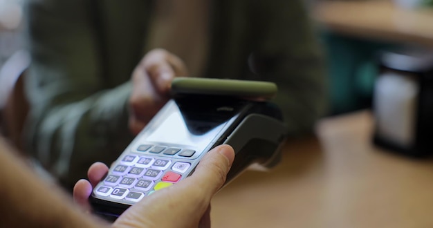 Primer hombre mano pagando con teléfono móvil a través de terminal pos con tecnología NFC Hombre usando teléfono inteligente para transferencia inalámbrica de dinero