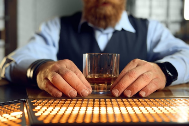 Foto primer hombre de negocios sosteniendo un vaso de whisky en la barra del bar. caballero pensando solo mientras descansa en el pub