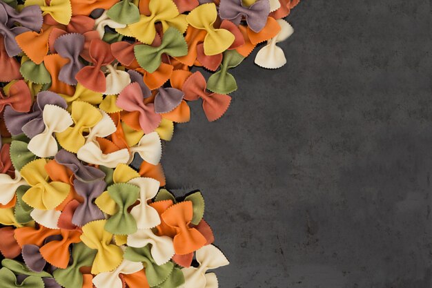 Primer italiano de las pastas farfalle multicoloras crudas en fondo negro con el espacio de la copia.