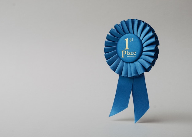 Primer lugar de roseta azul sobre un fondo gris como recompensa por logros, éxitos y victorias.