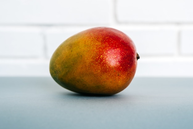 Primer mango fresco maduro colocado sobre la mesa contra la pared de ladrillo blanco en casa