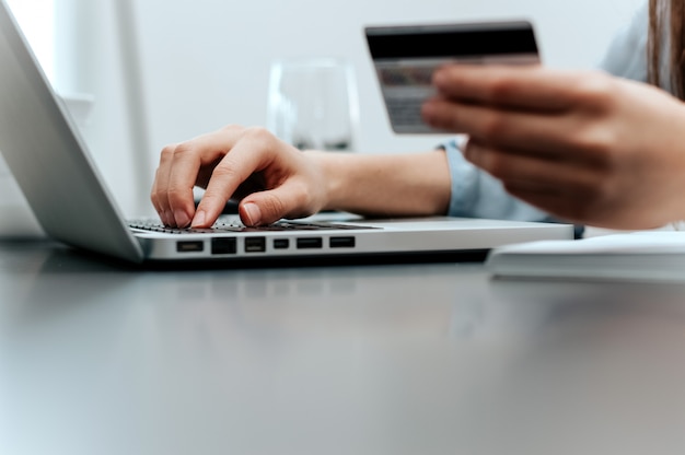 Primer de la mano femenina que sostiene la tarjeta de crédito y el ordenador portátil que hacen la compra de Internet.