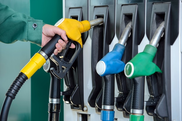 Foto primer de una mano del hombre que usa un surtidor de gasolina en una gasolinera.