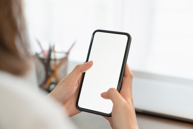 El primer de la mano de la mujer joven que sostiene el teléfono en la tabla y la pantalla es concepto en blanco, social de la red.