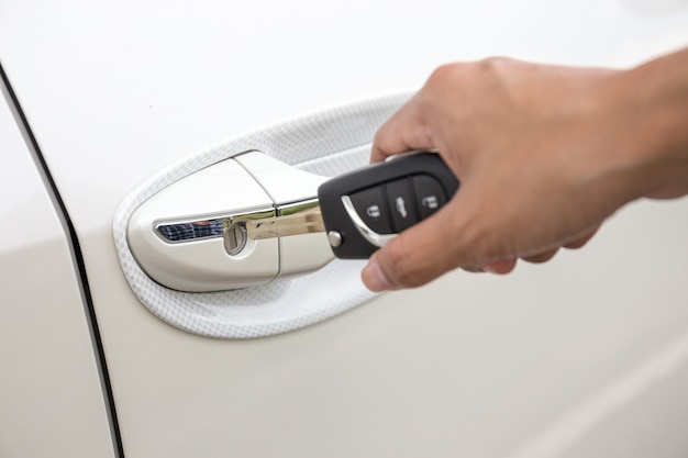 Primer de la mano de una mujer que inserta una llave en la cerradura de puerta de un coche blanco.