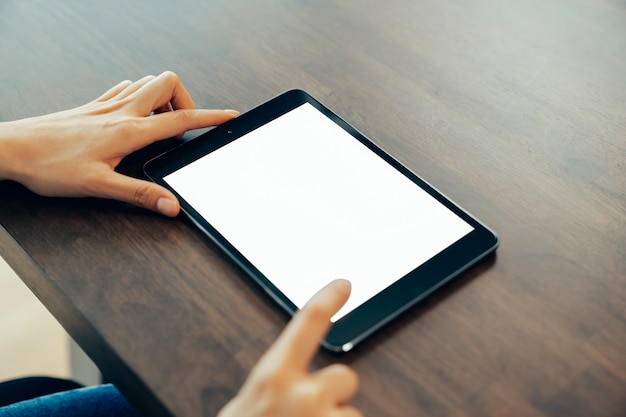 El primer de la mano de la mujer que sostiene la tableta digital en la tabla y la pantalla está en blanco.