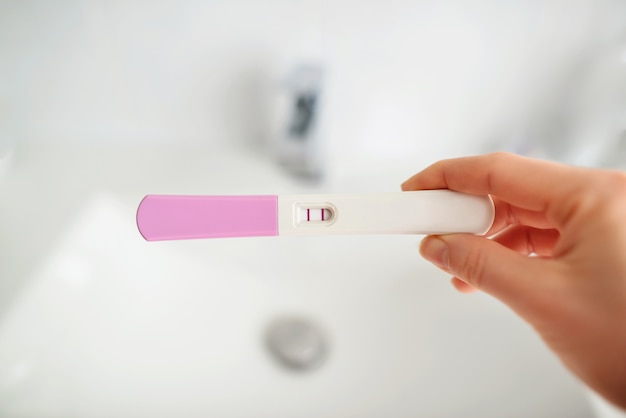 Primer mano de mujer sosteniendo la prueba de embarazo en el baño, concepto de atención médica, enfoque selectivo