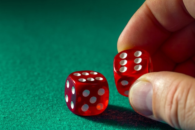 Primer de la mano que sostiene dados rojos con una combinación que gana en el paño verde en un casino.