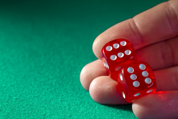 Primer de la mano que sostiene dados rojos con una combinación que gana en el paño verde en un casino.