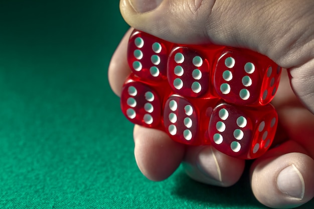 Primer de la mano que sostiene dados rojos con una combinación que gana en el paño verde en un casino.