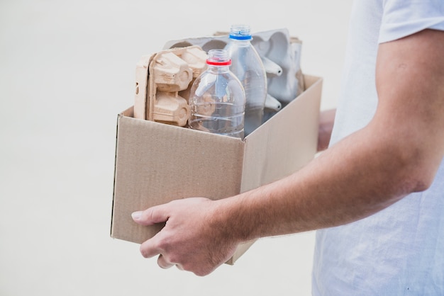 El primer de la mano que sostiene recicla la caja con el cartón del huevo y las botellas plásticas en el contexto blanco