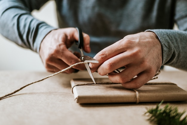 El primer de las manos masculinas que envuelven el presente con la cuerda natural y el papel del arte.