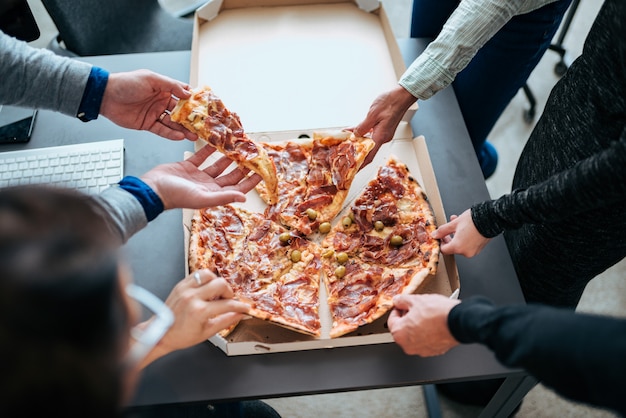 Primer de las manos que toman rebanadas de pizza en una hora de la almuerzo.