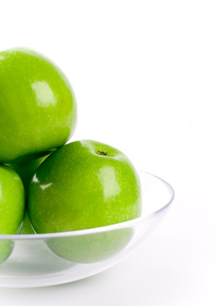 Primer de manzanas verdes en el tazón de fuente de cristal en el fondo blanco