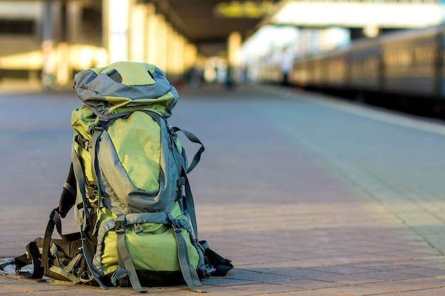 Primer de la mochila turística verde grande en la plataforma de la estación de tren. Concepto de viaje, aventura y recreación.