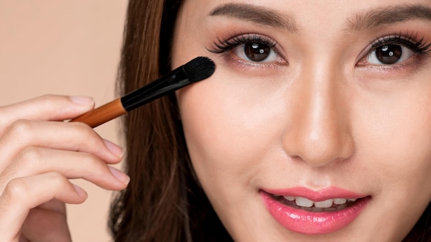 Primer modelo femenino ardiente aplicando su sombra de ojos y sosteniendo un espejo
