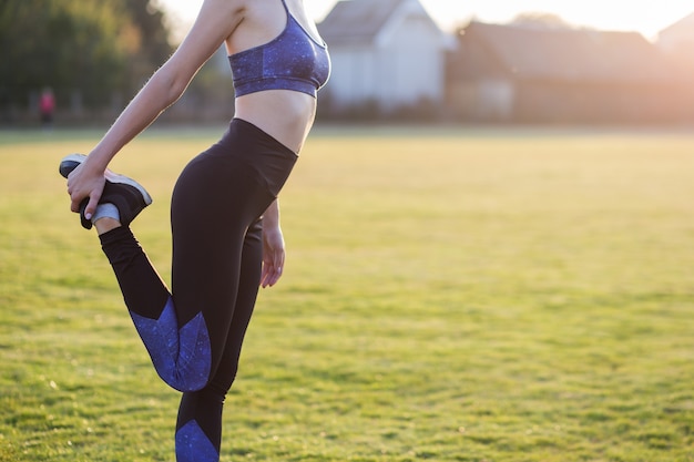 Primer de la mujer deportiva joven que hace ejercicio antes de correr en campo de la mañana al aire libre.