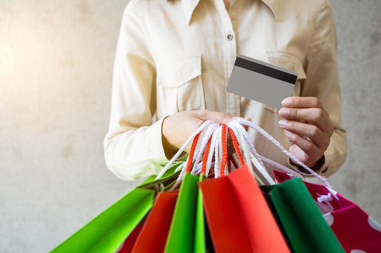 Primer de la mujer que sostiene bolsos de compras y que usa una tarjeta de crédito.