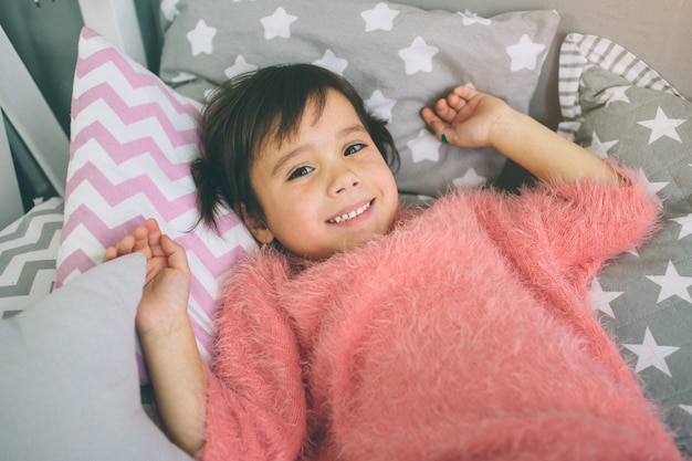 Primer de la niña linda en ropa rosada en la cama. descansar en casa