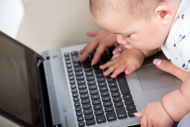 El primer niño pequeño dulce está jugando con la computadora portátil.