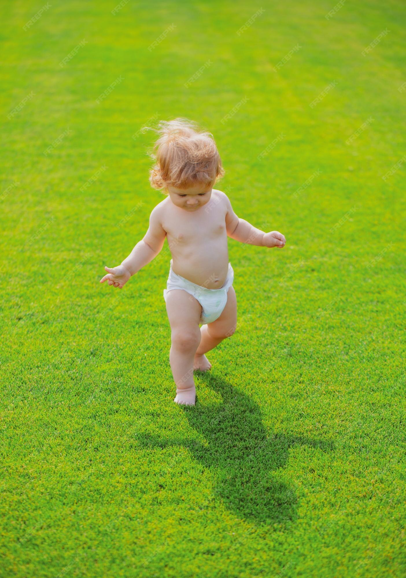 Primer paso bebé niño pequeño caminando un parque en un día de primavera bebé piernas desnudas pie en verde | Foto Premium