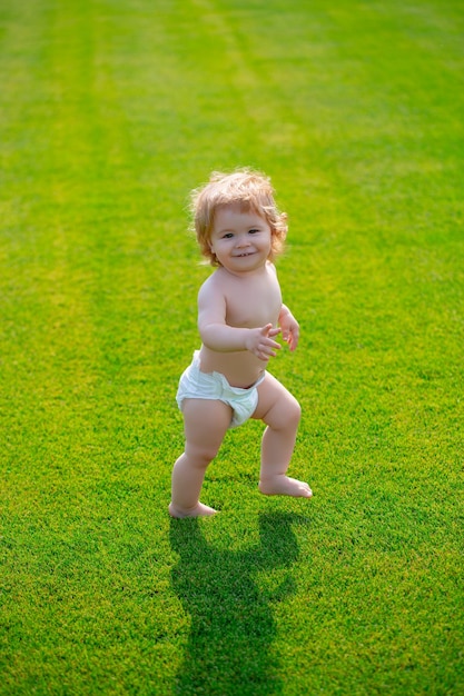 Primer paso bebé de pie descalzo sobre el césped verde en pantalones de pañales hermoso niño feliz walki