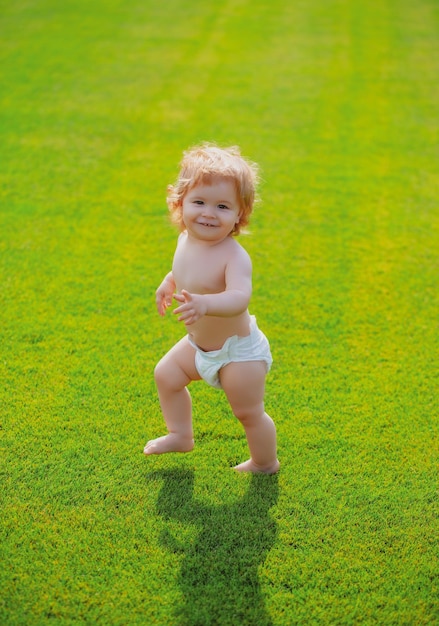 Primer paso bebé de pie descalzo sobre el césped verde en pantalones de pañales hermoso niño feliz walki