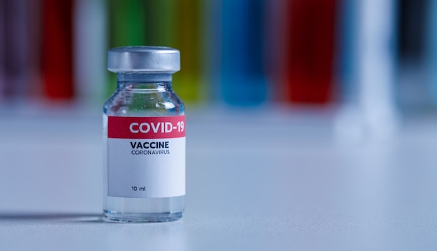 Primer plano de 10 ml de vacuna contra el coronavirus covid 19 en un frasco de vidrio pequeño con etiqueta roja para la prevención de la protección, el brote epidémico de virus pandémico en todo el mundo en el laboratorio con fondo borroso.