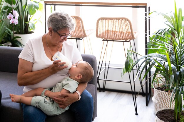 Primer plano de una abuela alimentando con un biberón a su nieto en casa