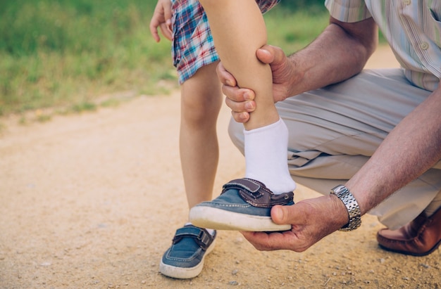 Primer plano del abuelo poniendo zapato a su nieto sobre un fondo de vía natural