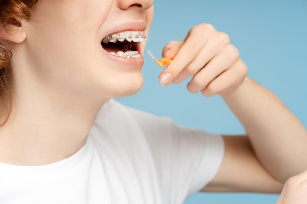 Foto primer plano de un adolescente rizado con aparatos ortopédicos sosteniendo un cepillo de dientes cepillándose los dientes en el baño