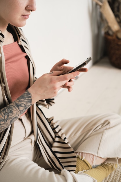 Primer plano de una adolescente sentada en el suelo y usando su teléfono móvil ella hablando en línea