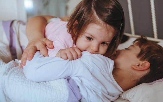 Primer plano de una adorable niña jugando con un niño acostado en la cama con su madre en una mañana relajada. Concepto de tiempo de ocio familiar de fin de semana.