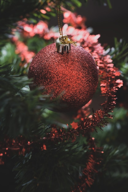 Primer plano de adorno navideño rojo brillante colgando de un árbol de Navidad decorado con cinta brillante.