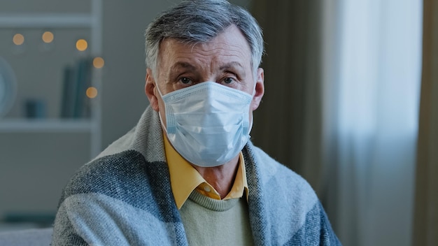 Primer plano adulto hombre maduro con máscara médica mirando a la cámara hombre viejo enfermo sentado en el interior