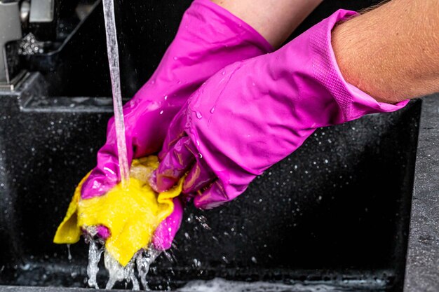 Un primer plano del agua que fluye del grifo y un hombre con guantes y un trapo