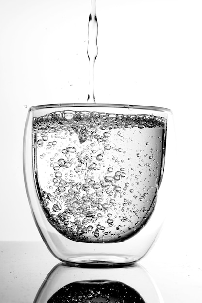 Foto primer plano de agua que se vierte en vidrio contra un fondo blanco