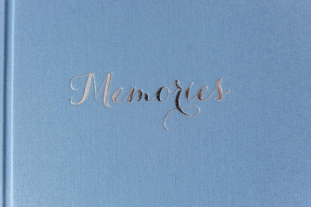 Primer plano del álbum de fotos cerrado sobre una mesa de madera blanca Álbum de bodas azul con relieve plateado