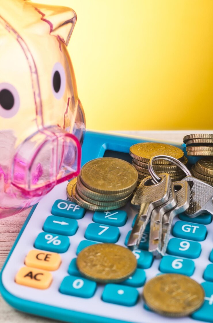 Foto primer plano de una alcancía con monedas y llaves en una calculadora contra un fondo amarillo